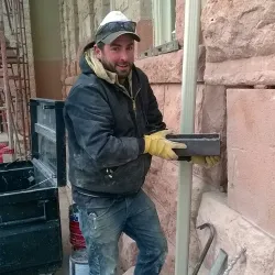 Michael Madone of Mountain masonry pulling out a time capsule from behind some stone masonry